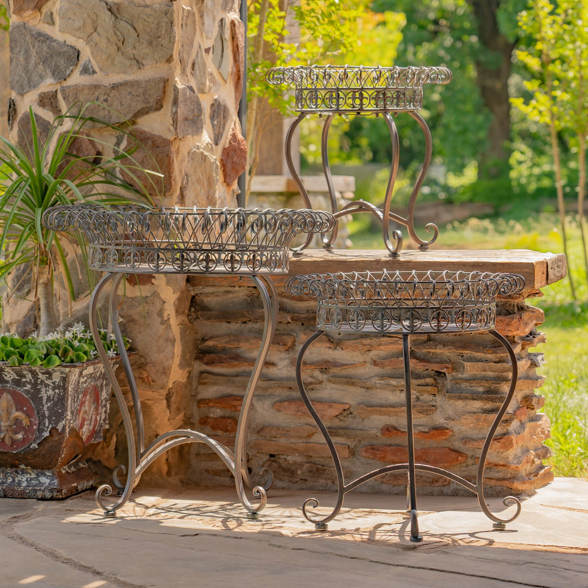 Three ornate basket stands grouped beside a stone ledge, showing their curved legs and open wire trays.