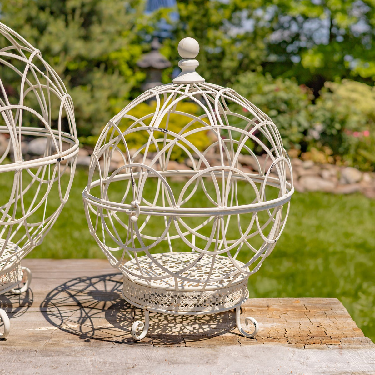 Antique white wire globe plant stand shown outdoors beside a wooden table