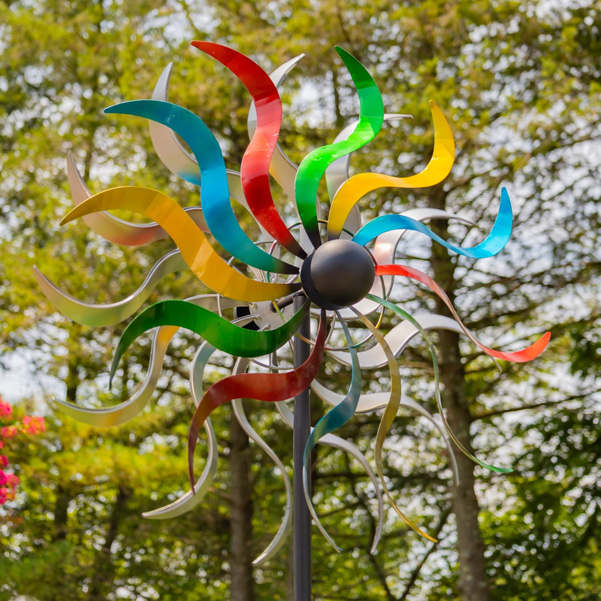 The wind spinner’s bright curved metal blades fill the frame against a leafy backdrop.