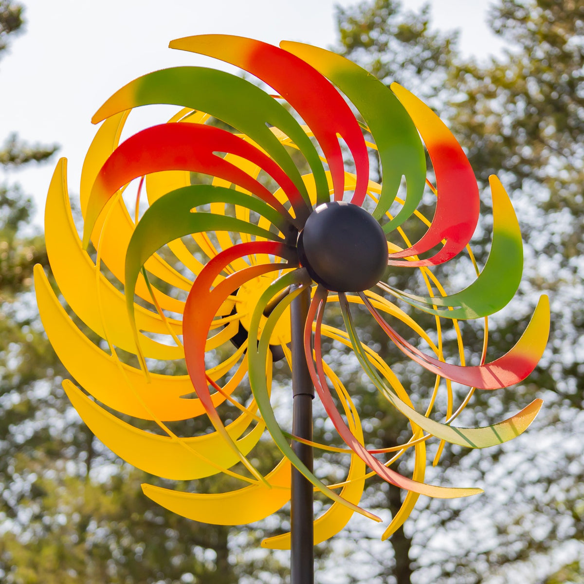 The colorful curved blades fan around the central hub, with trees visible behind them.