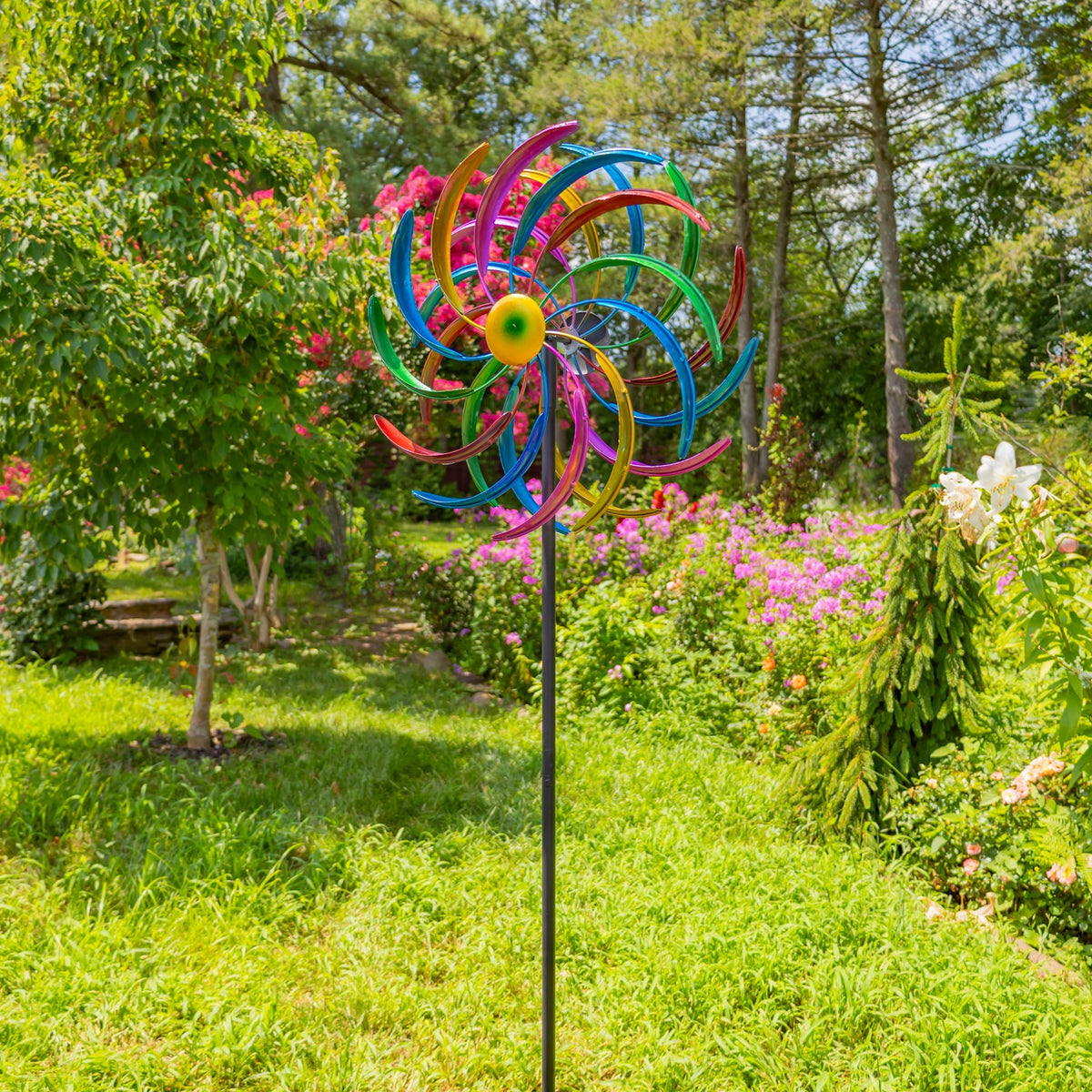 Full-height windmill stake standing in a green garden with flowering shrubs