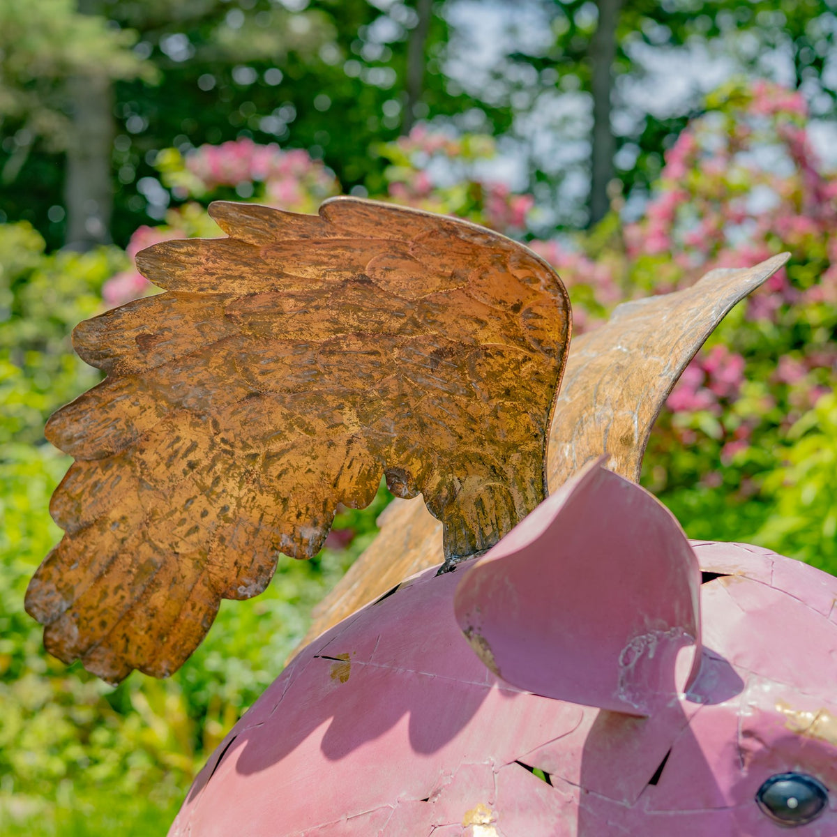 Close-up of a large textured, gold-toned metal wing above the pig’s pink back and ear.