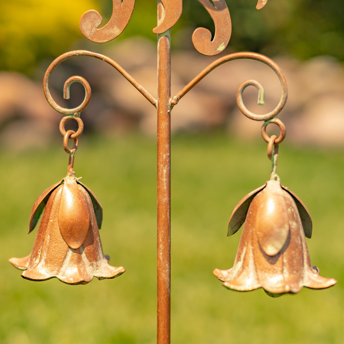 Two metal lily-shaped bells hang from curled arms beside the stake’s central rod.