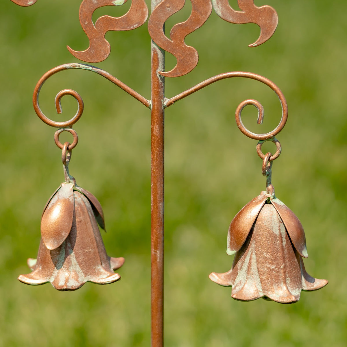 Two flower-shaped metal bells hang from curled arms on the garden stake.