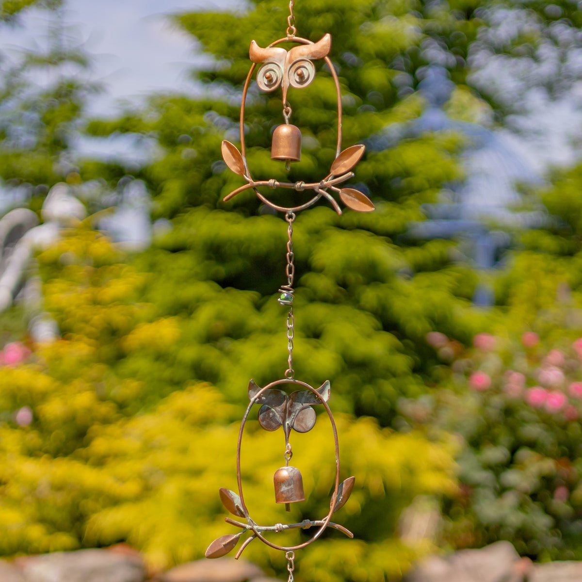 Two owl-shaped links with small bells and leaf details shown against a garden backdrop.