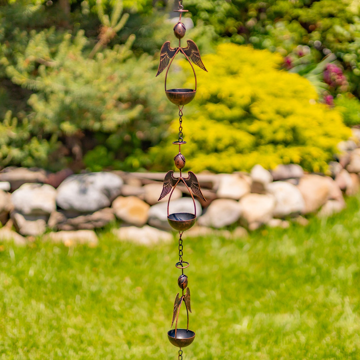 Several winged angel ornaments and bowls repeat along the hanging rain chain in a garden.