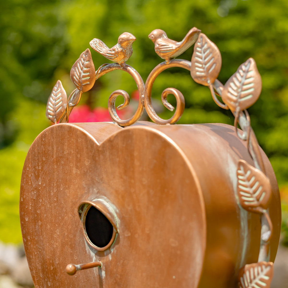 Close-up of two small bird figures and curled metal scrolls above the birdhouse entrance.