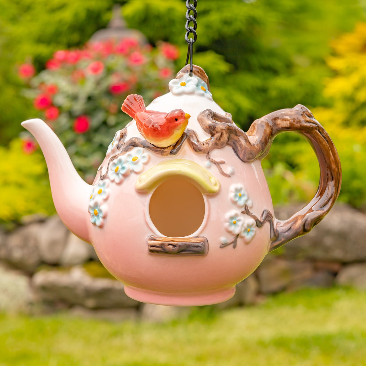 Pink teapot birdhouse with a red bird, tiny flowers and raised brown trim hanging from a chain