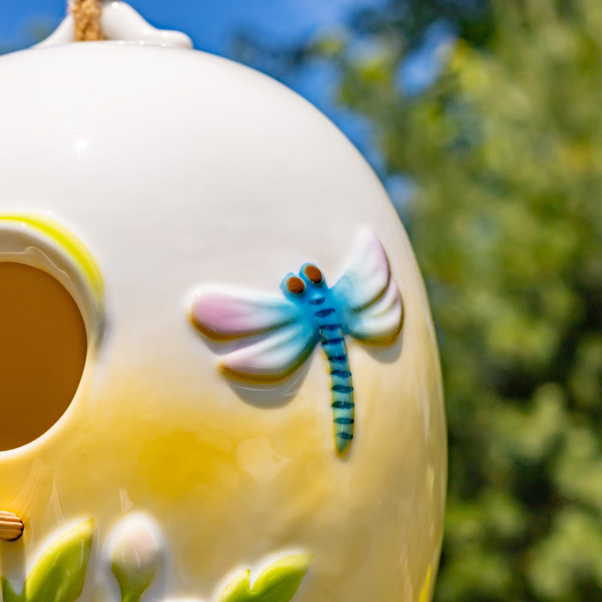 Raised blue dragonfly with pink and white wings on the birdhouse’s glossy yellow surface.