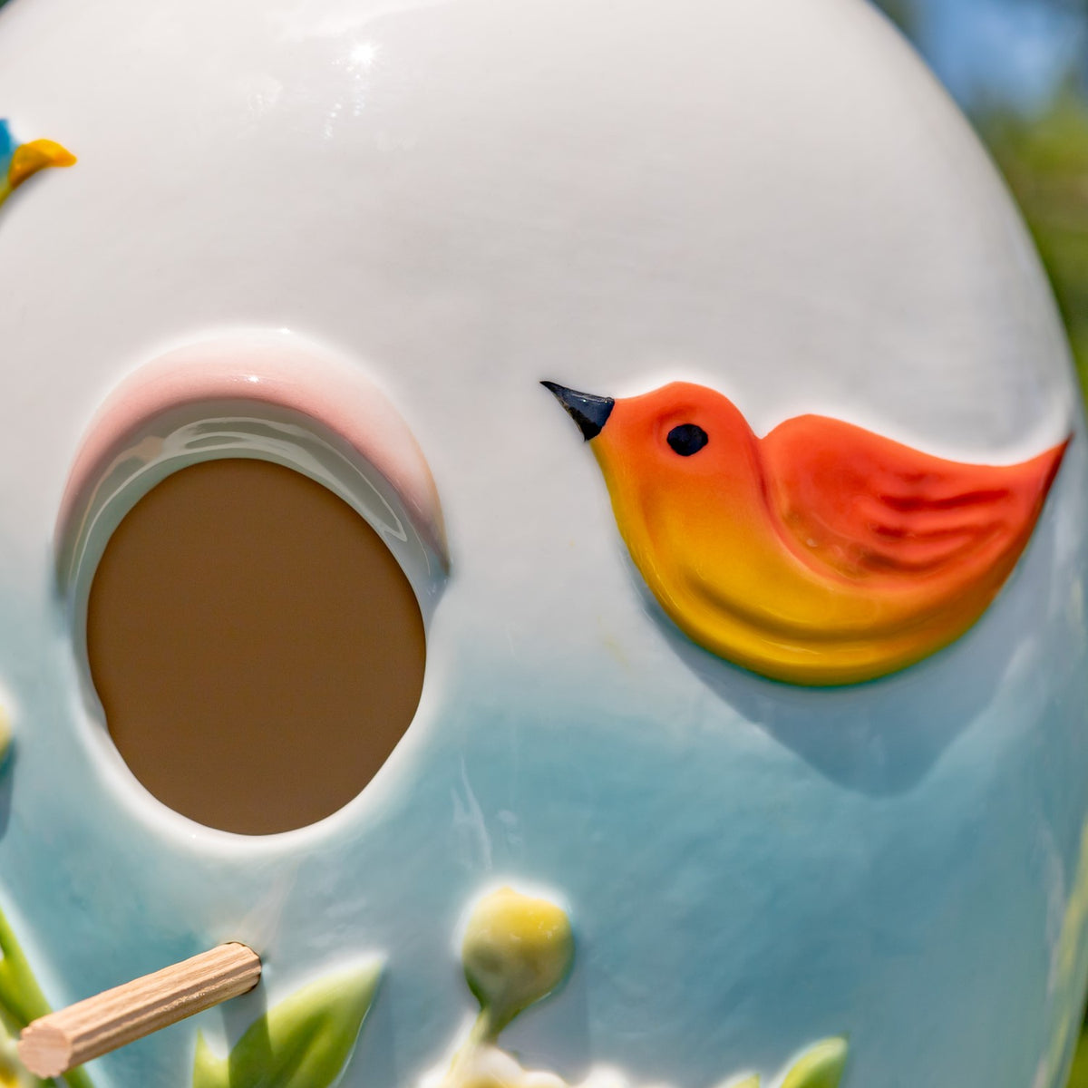 Close-up shows a raised orange bird beside the birdhouse entrance and a small perch below.