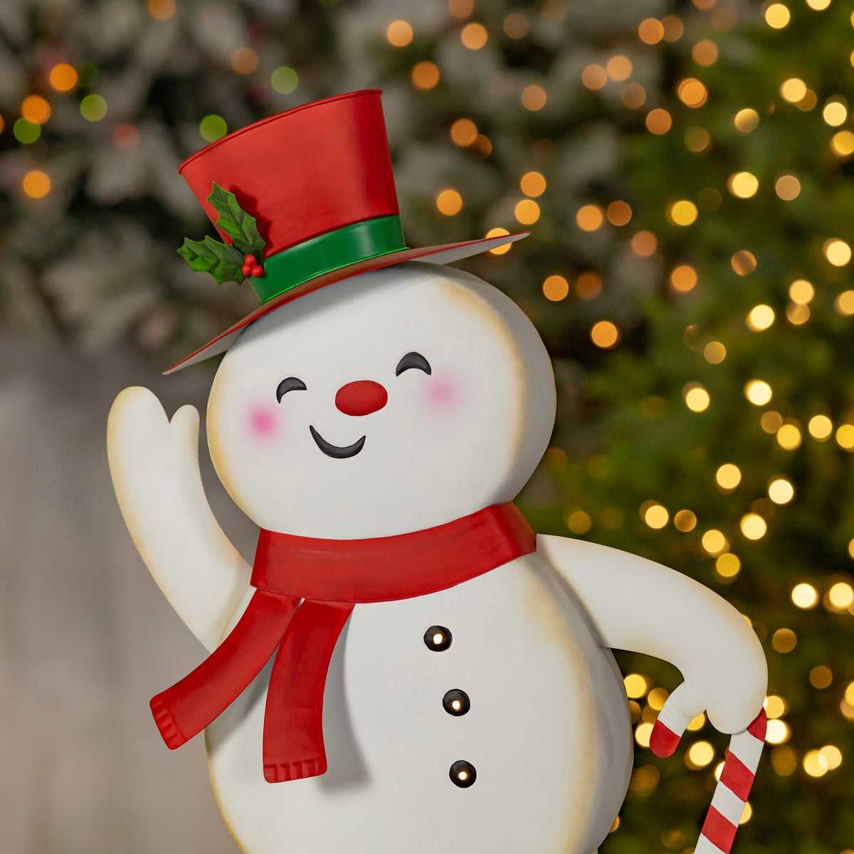 Close view of a smiling snowman’s red scarf, top hat, raised arm and candy cane.