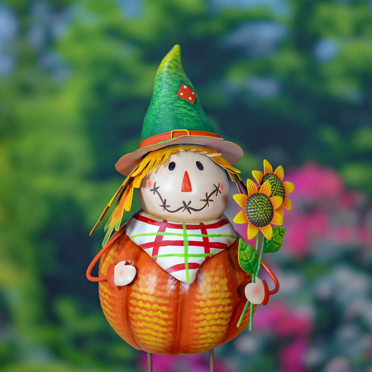Close-up of a pumpkin scarecrow’s stitched face, green hat, plaid scarf and sunflower.