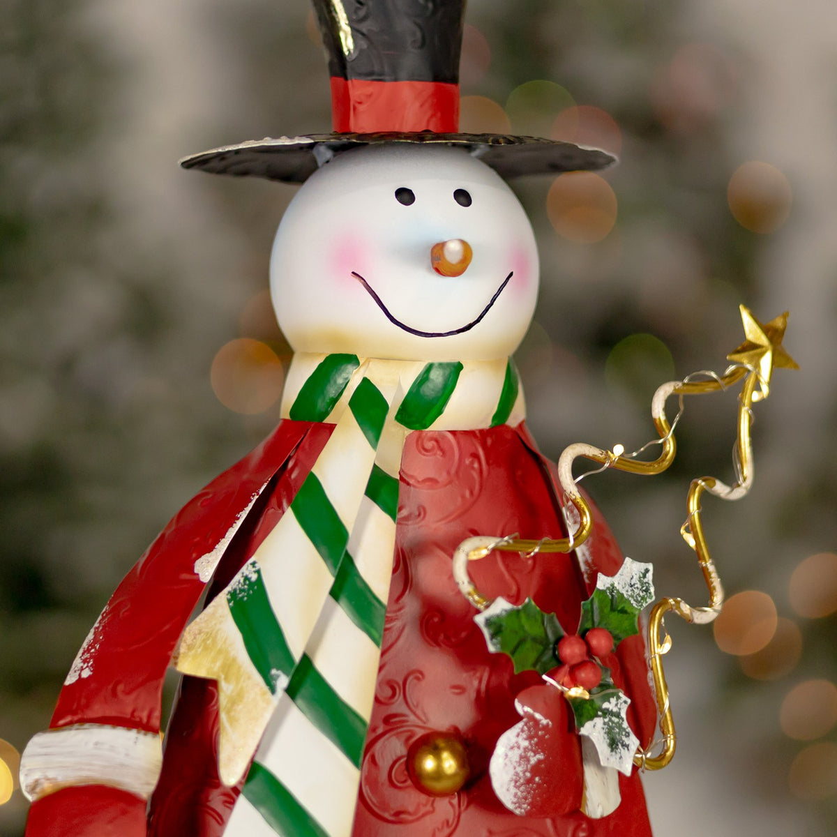 Close view of the red snowman's smiling face, scarf, holly decoration and gold wire star.