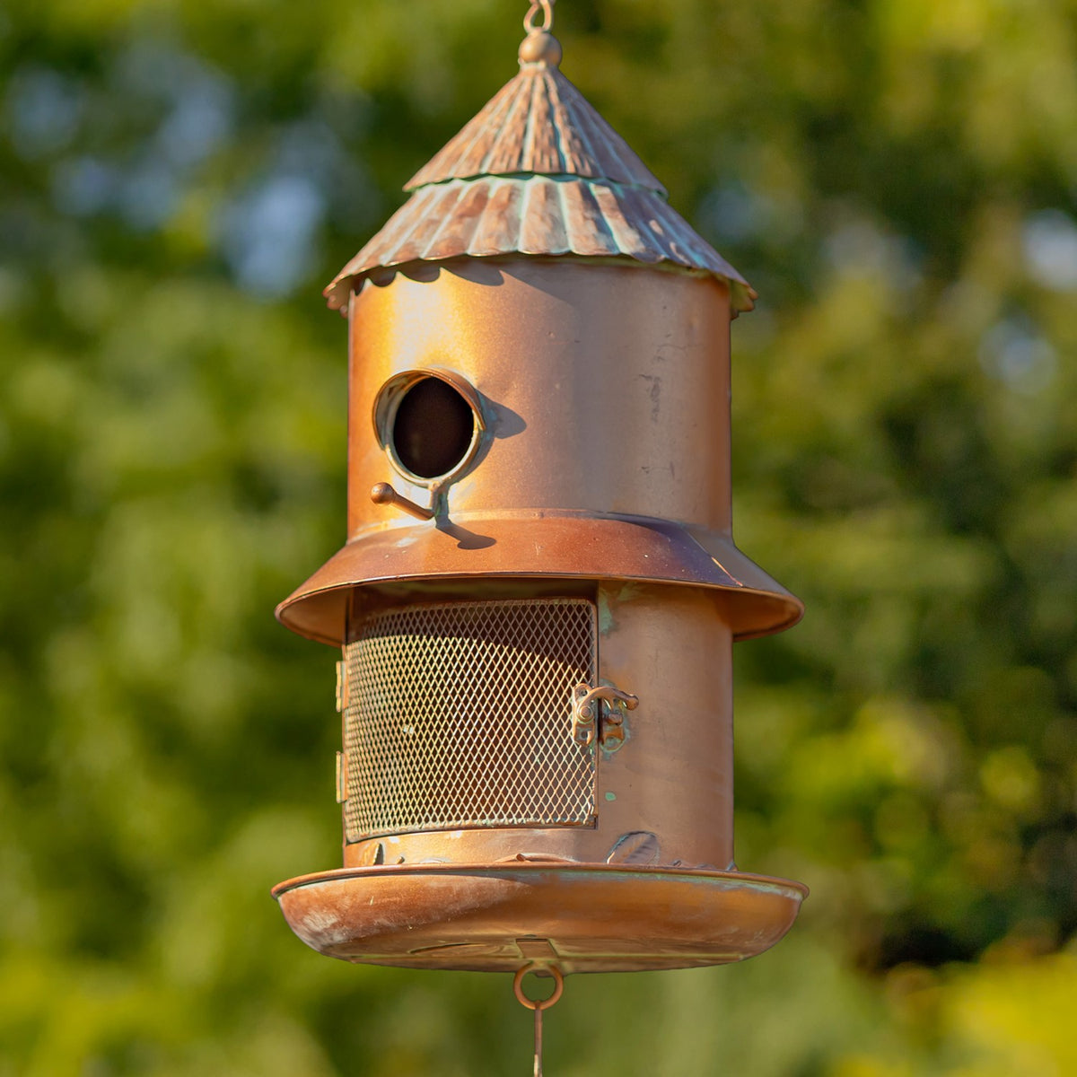 Copper-toned hanging feeder with a tiered pointed roof, circular bird opening, and wire-mesh seed compartment.