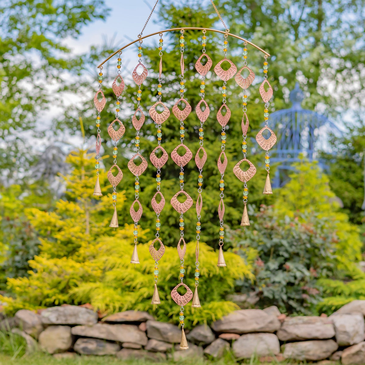 Pink-toned openwork ornaments dangle from a curved chime frame with beads and gold-toned bells.