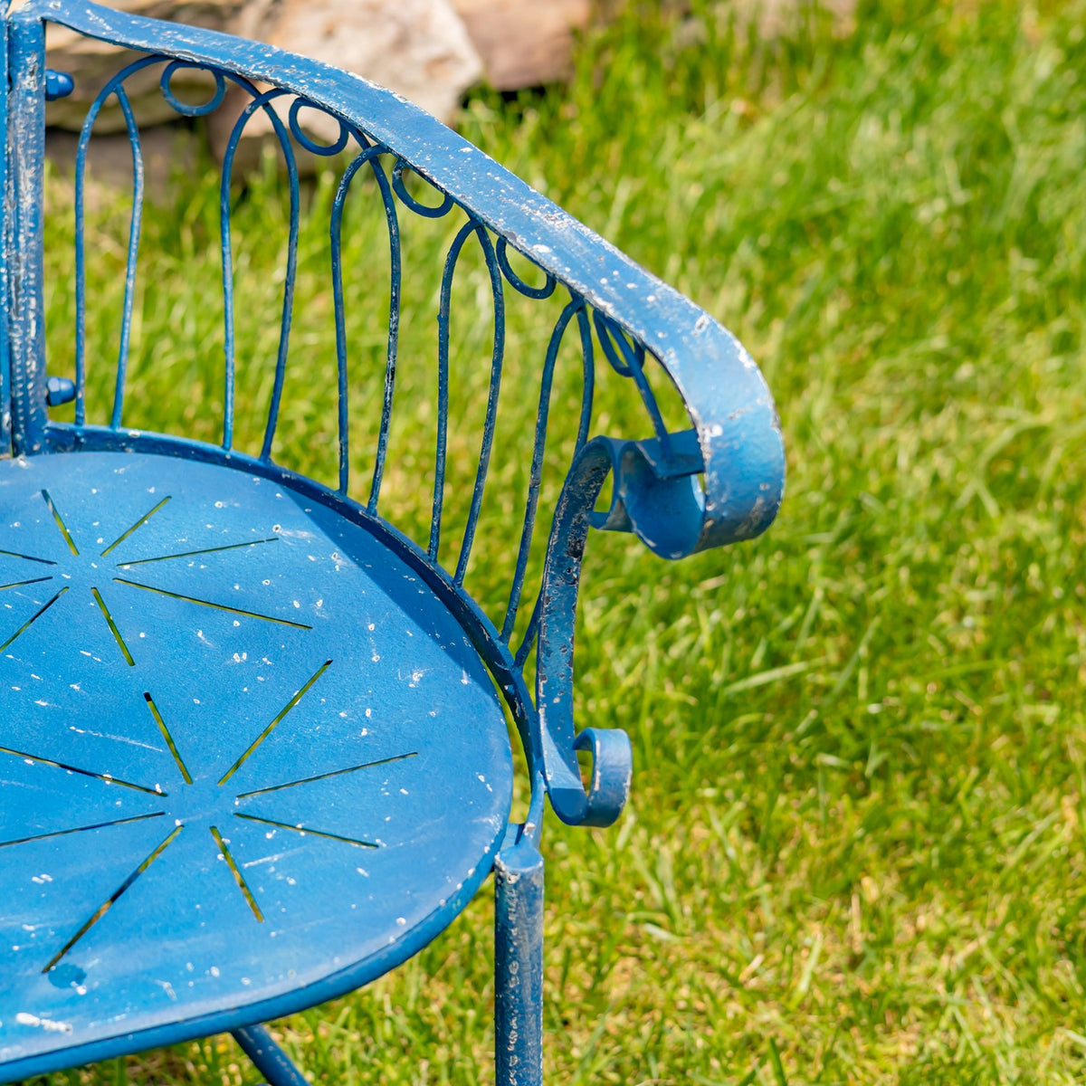 Close-up of the blue iron bench's curled armrest and decorative metal seat