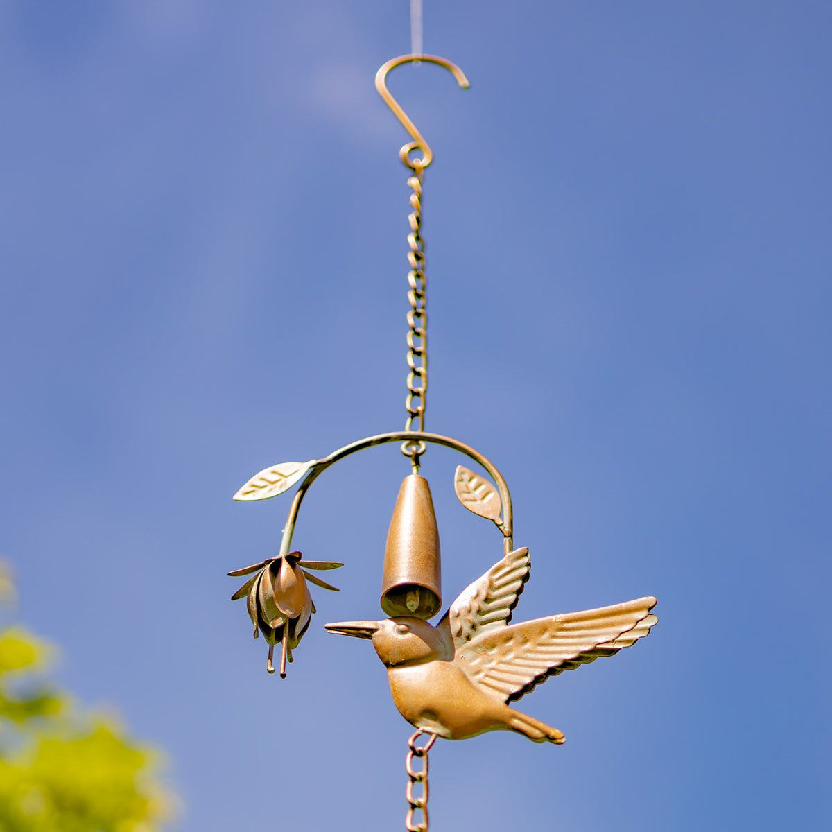 A curved hanging hook supports a chain and close-up hummingbird ornament against blue sky.