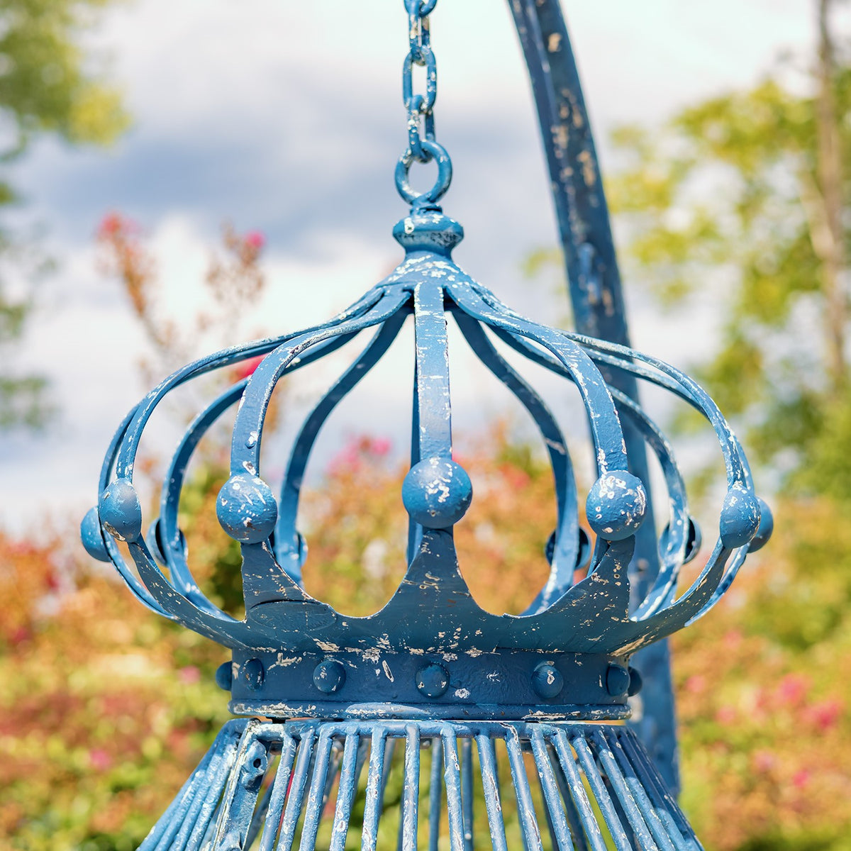 Close-up of the blue metal chair’s crown, curved bars, and hanging chain.