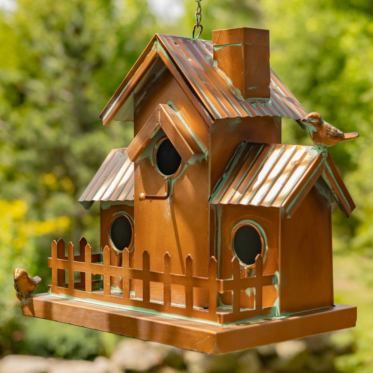Opposite side of the copper-colored birdhouse, showing its chimney-like detail, round openings, and fence.