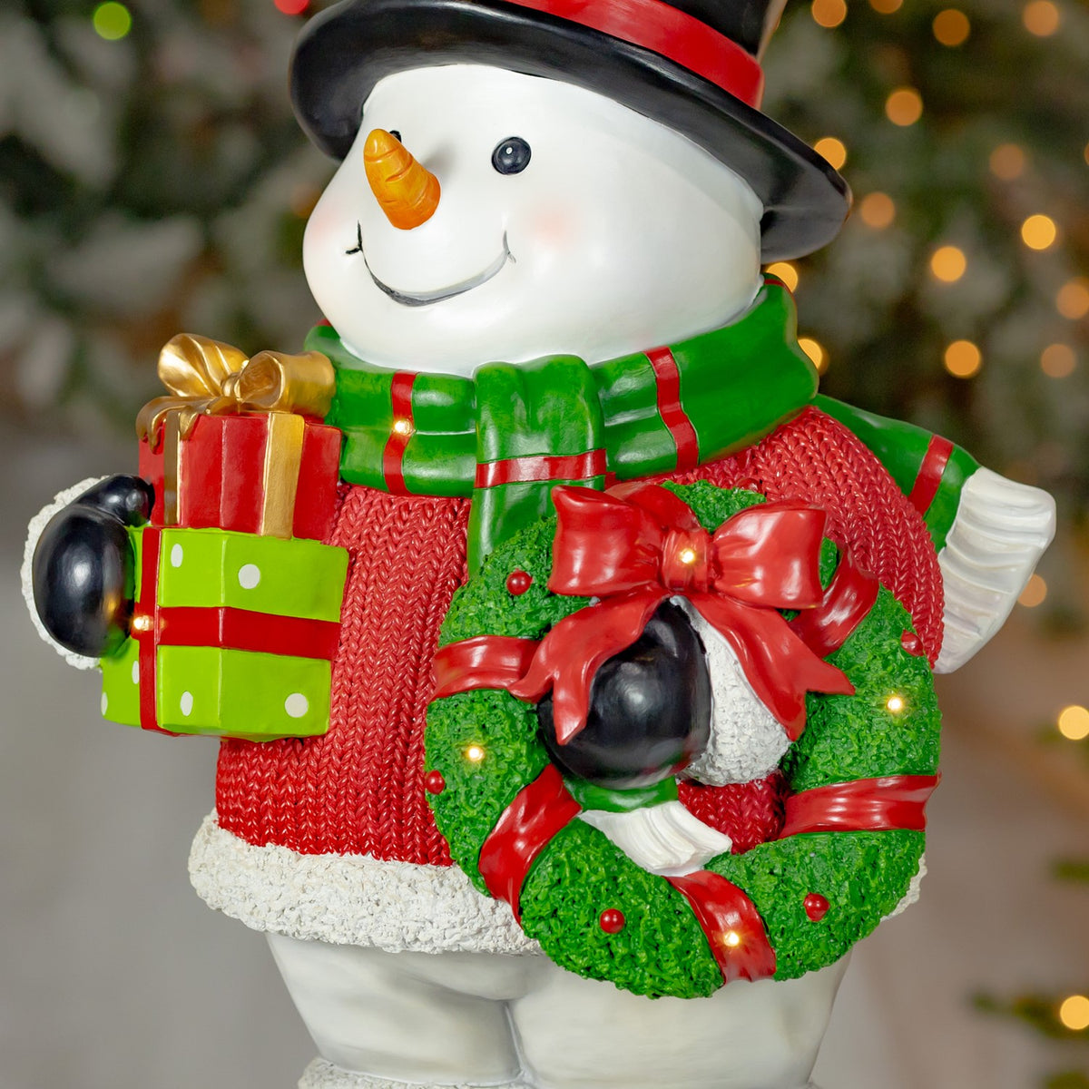 Close view of the snowman's red-bowed green wreath, stacked gifts and textured red sweater.
