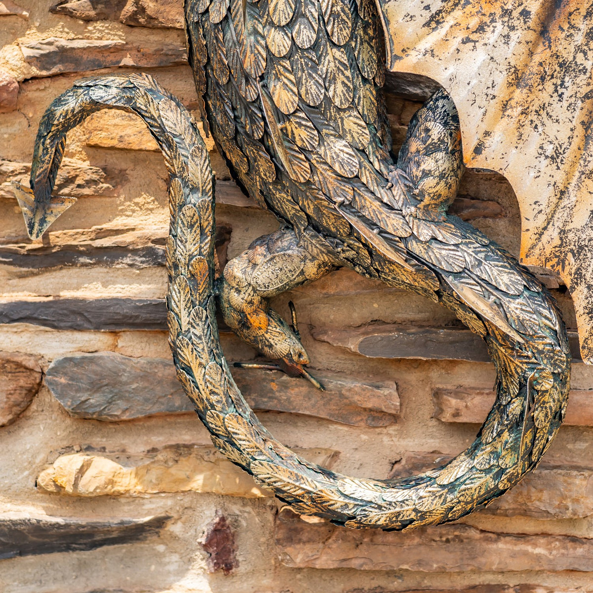 Close-up of the dragon’s curled, scaled tail and feet against the stone backdrop.