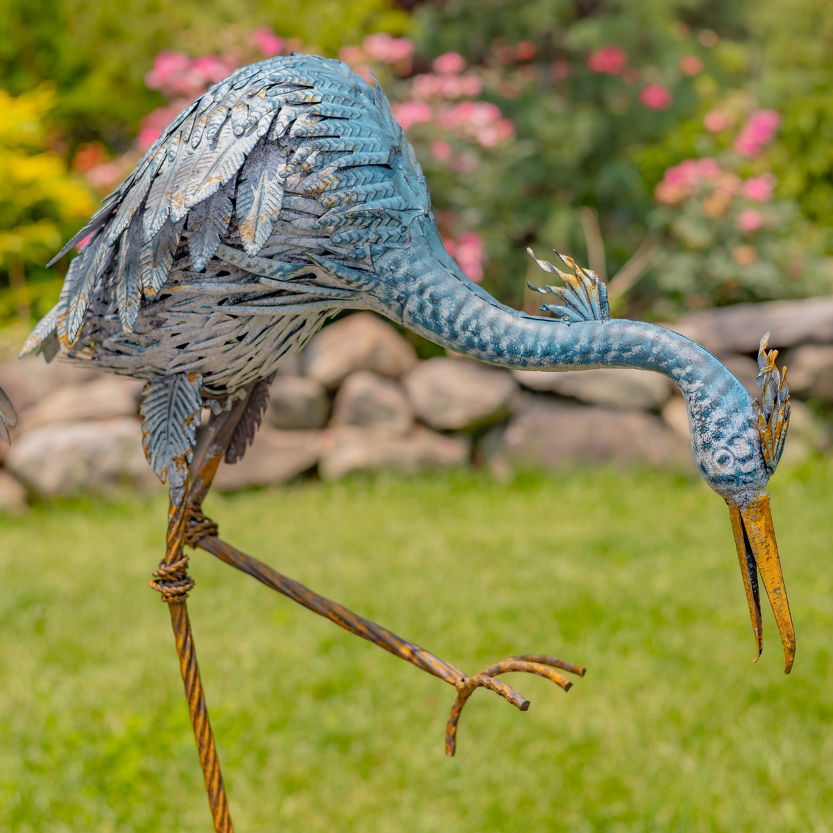 Side view of a blue and grey heron figurine bending toward the ground