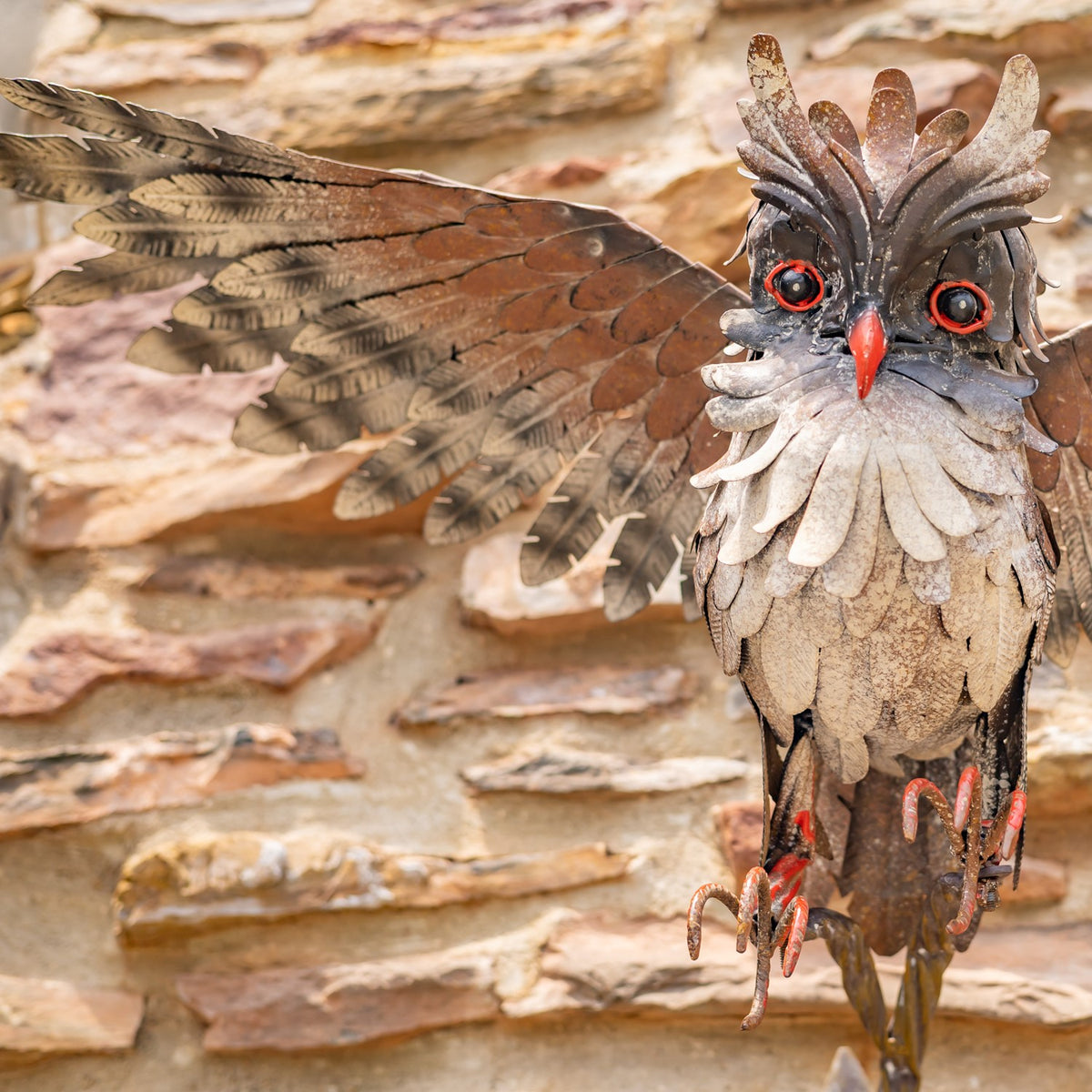 Close-up of the owl's layered metal feathers, bright eyes, red beak, and extended wing.