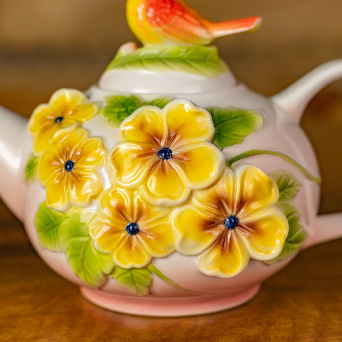 Raised yellow flowers with dark centers and green leaves decorate the teapot body.