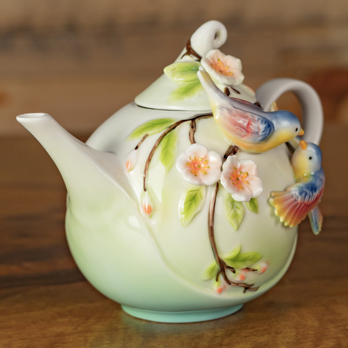 Teapot side with a long spout, painted flowering branch, and raised birds near the lid and handle.