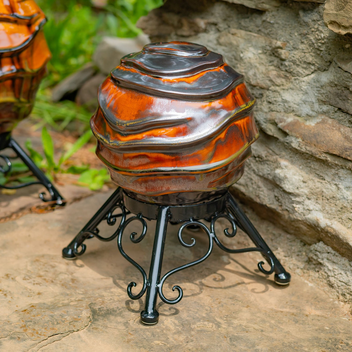 A smaller-looking orange and gray globe on a black scrollwork stand beside a stone wall.