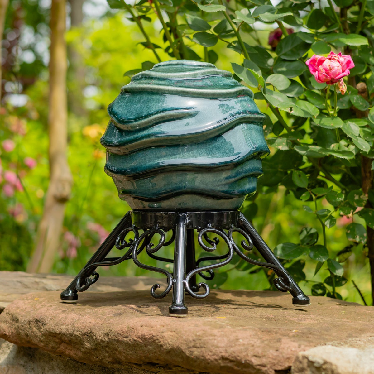 A teal globe on a decorative black stand rests on a stone ledge beside a pink rose.