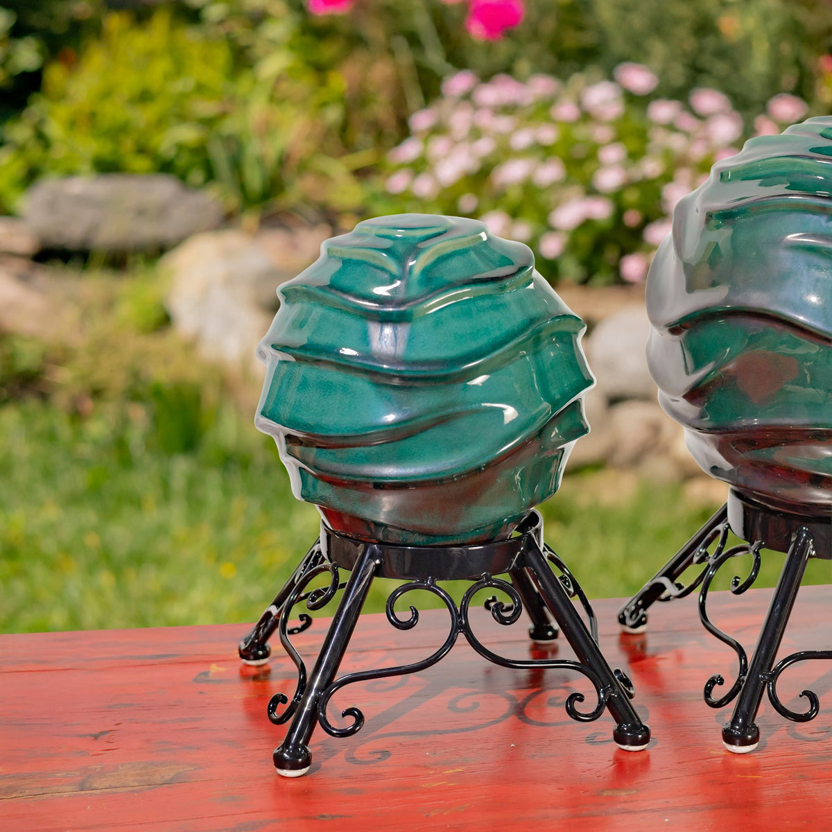 A small glossy teal globe on a black scrollwork stand is shown beside part of a larger globe.