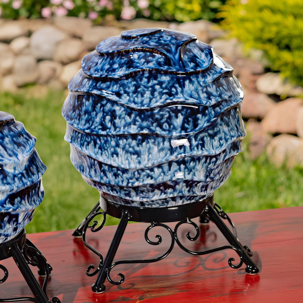 Close view of a blue-and-white ridged globe and its curled black metal stand.