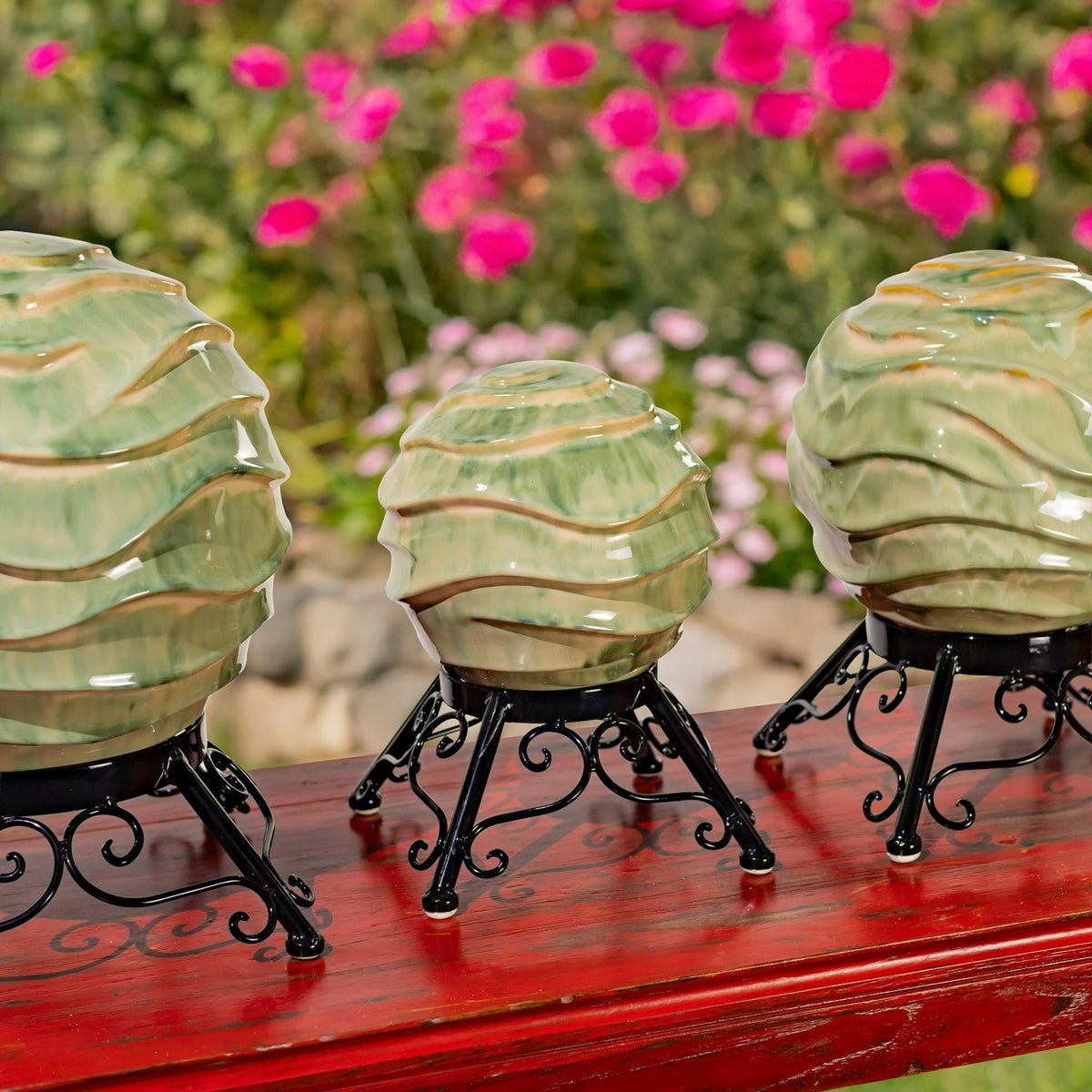 Three pale green wavy-banded globes on black stands, viewed at an angle across a red tabletop.