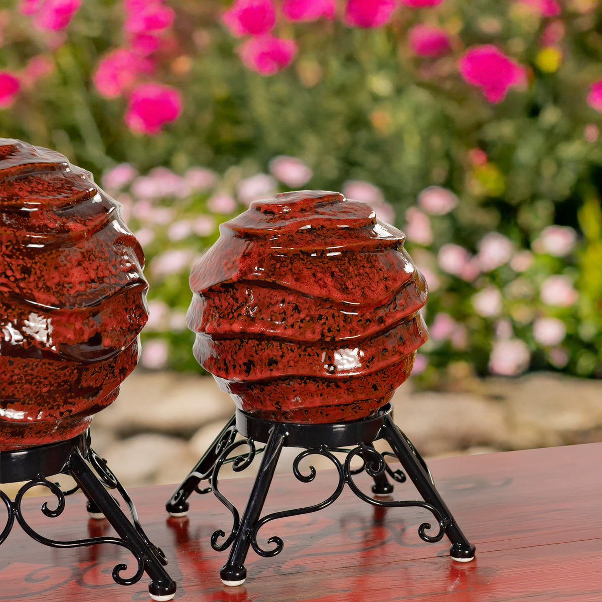 A glossy red ridged globe on a curled black metal stand, with part of another globe at the edge.