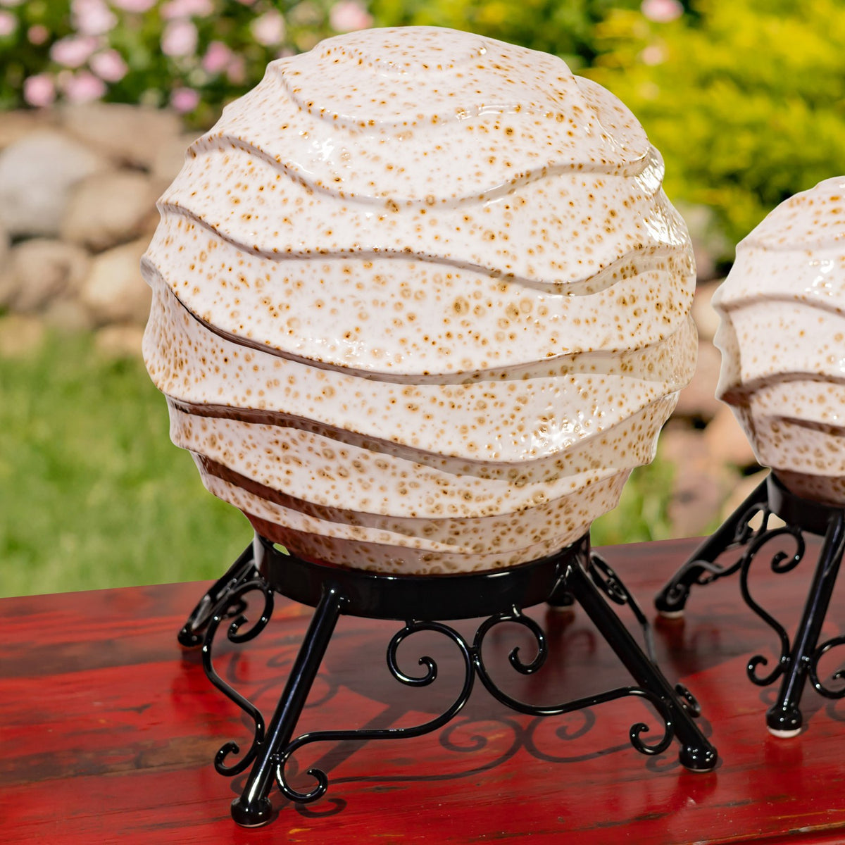 Close view of a speckled ivory globe with layered ridges on an ornate black stand.