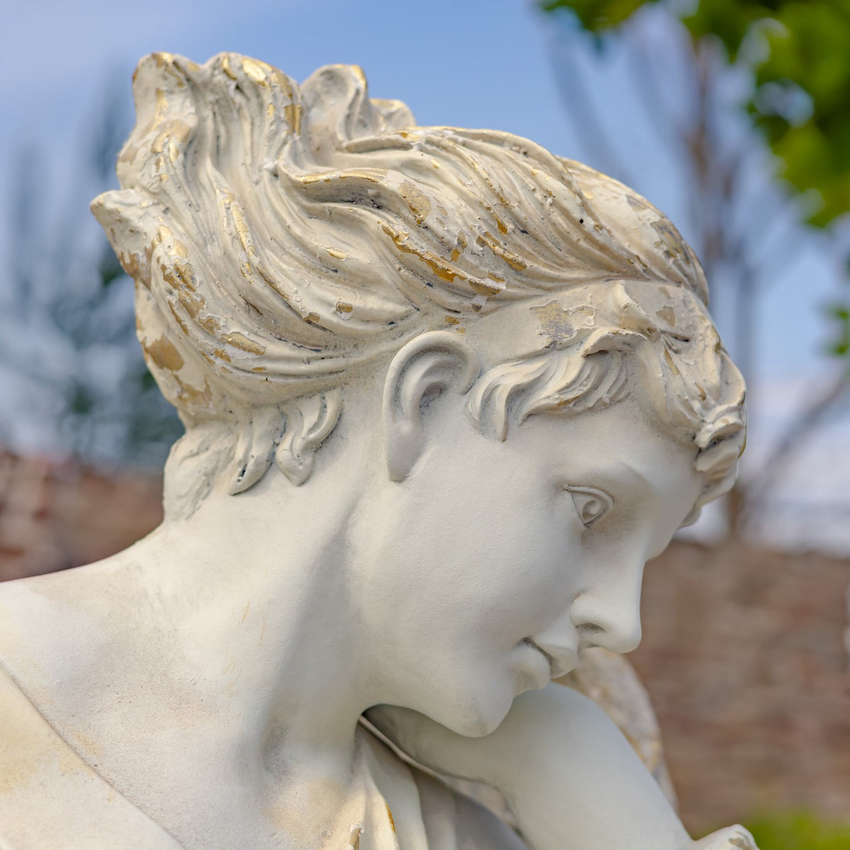 Side close-up of the angel’s downcast face and sculpted curls, showing a distressed finish.