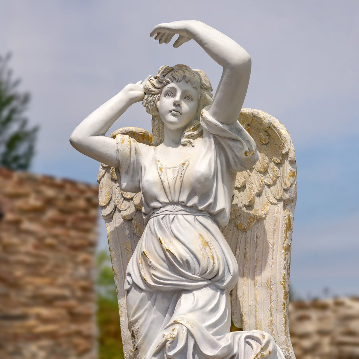 Angel statue shown from the waist up against the sky, with detailed wings and raised arms.