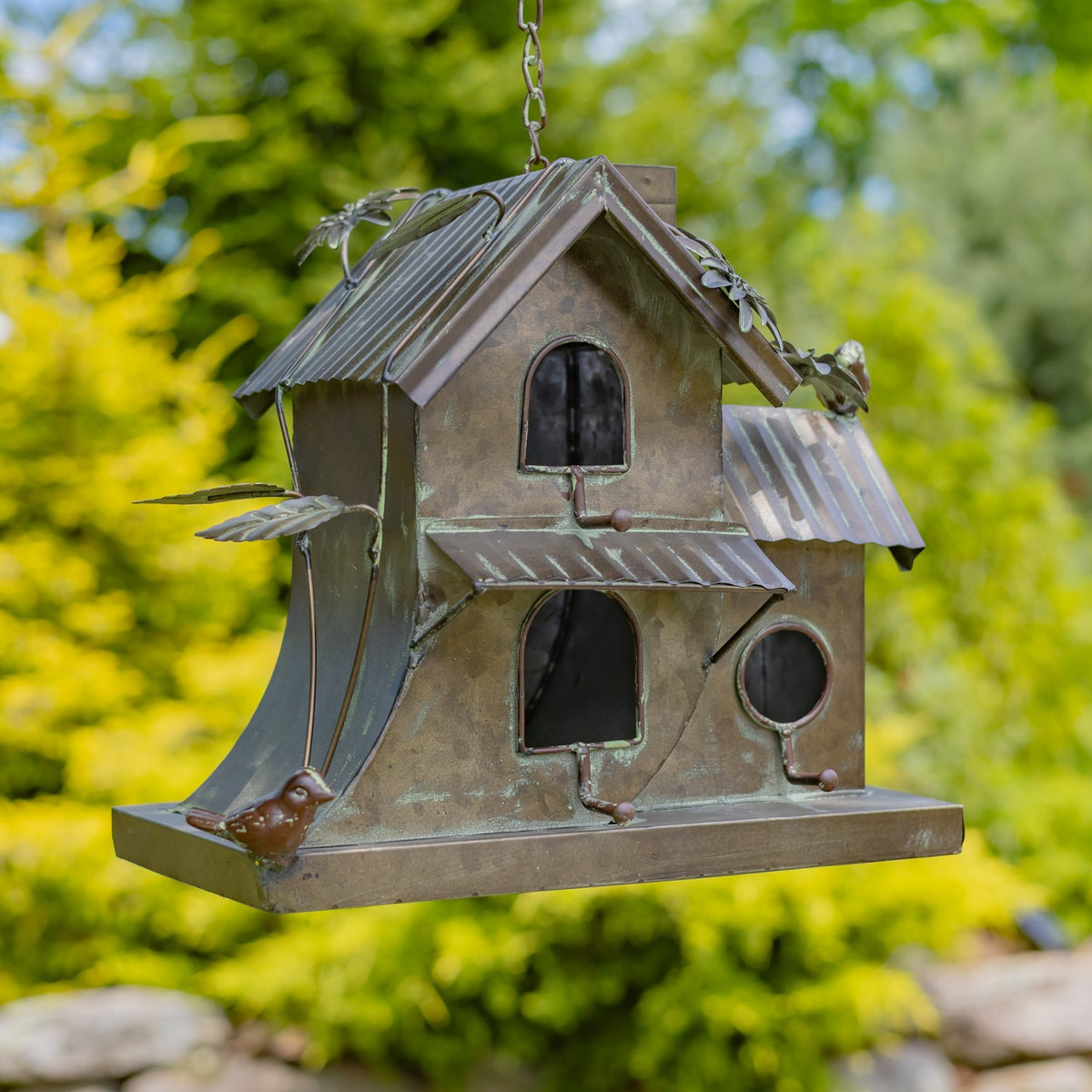 Close angled view of a metal birdhouse with mixed arched and round entrances, roof awnings, and bird ornaments.