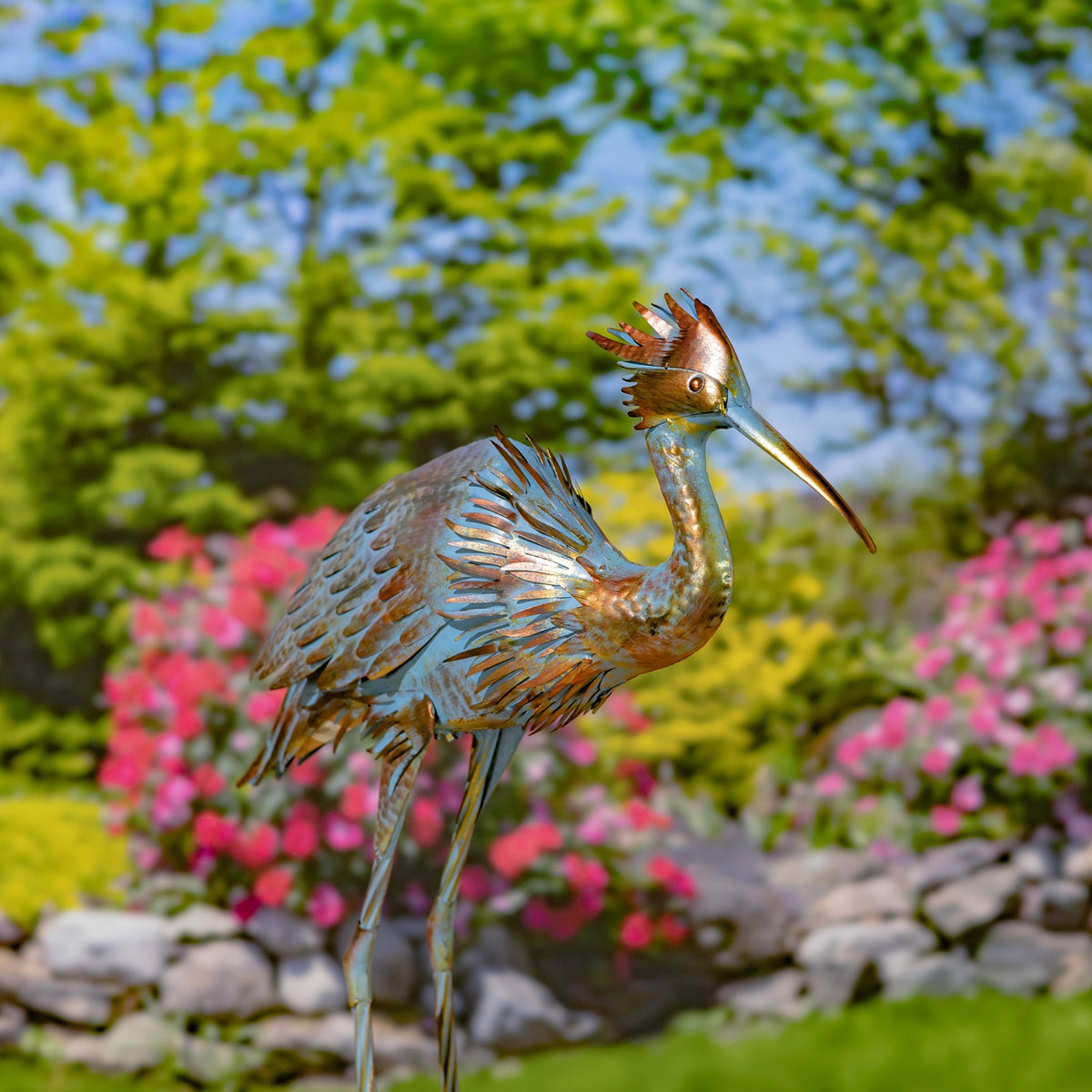 Metal heron garden sculpture standing with folded wings and its beak pointing right.
