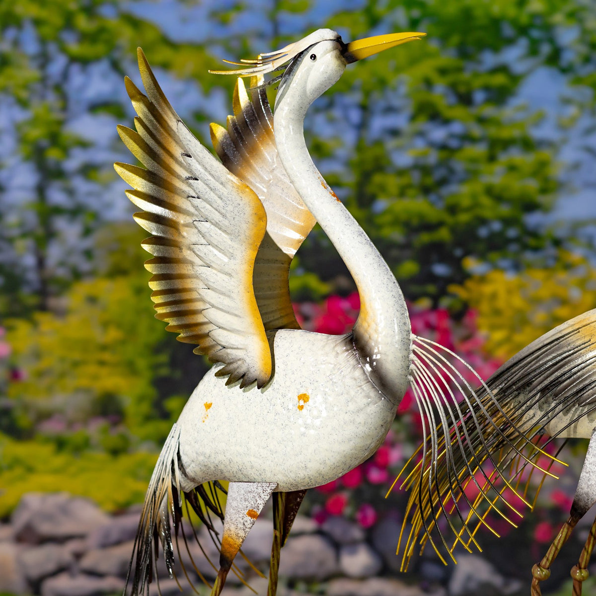 One heron figurine fills the frame with a raised wing, slender legs, and fine metal feather strands.