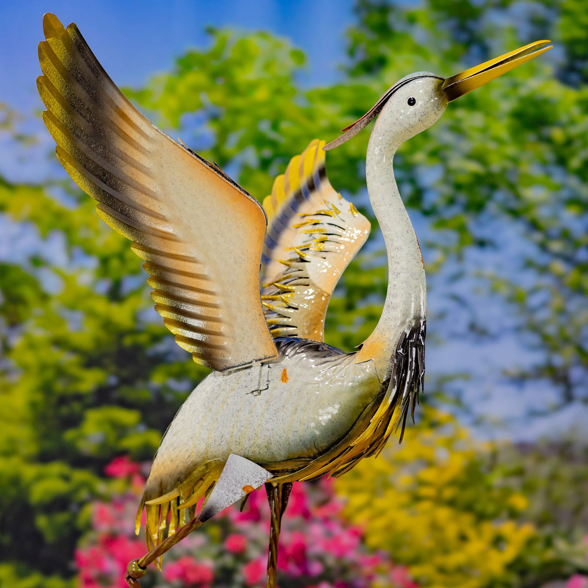 Close-up of a crane figurine with a raised wing, long yellow bill, and layered metal feather details.