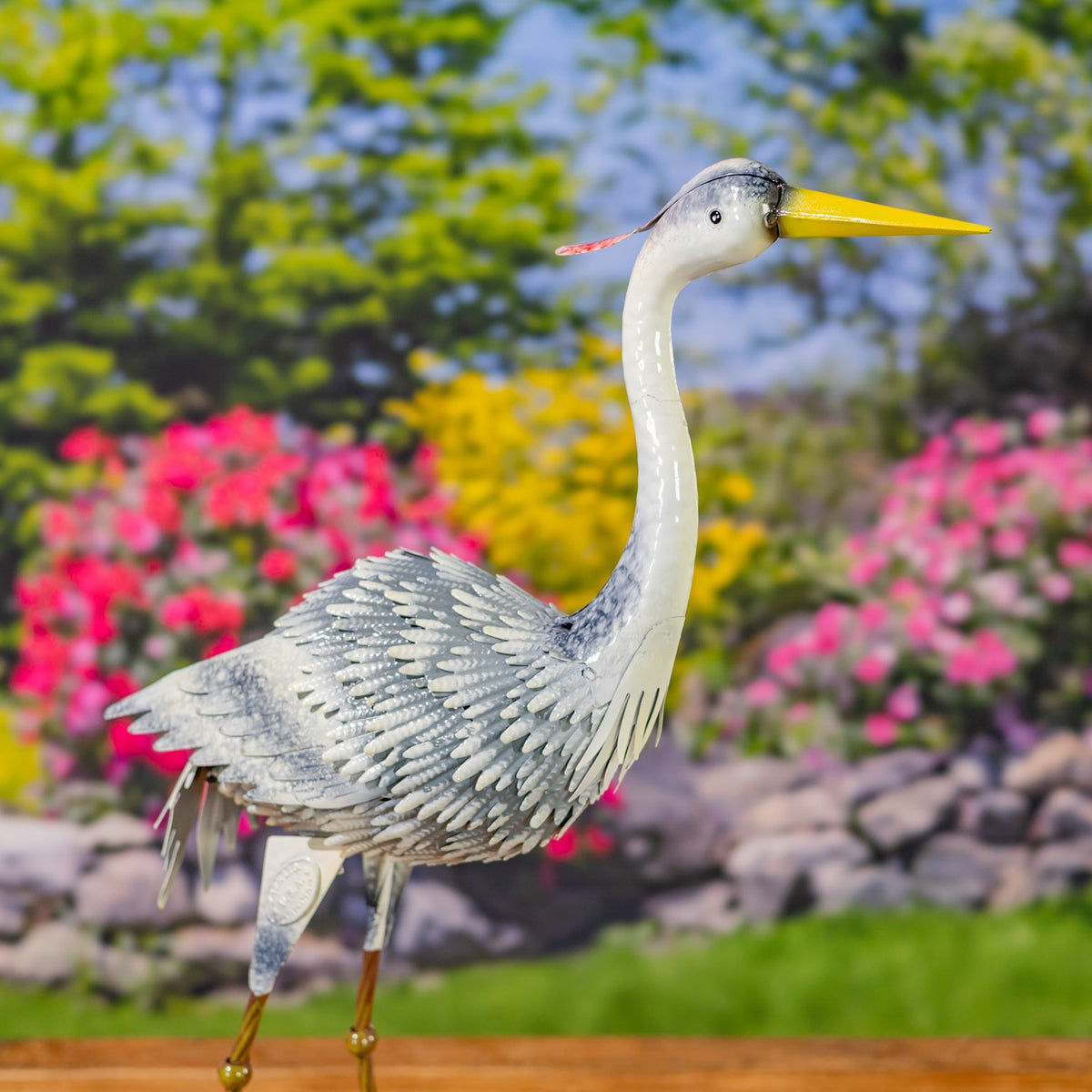 A metal heron figure stands in profile with a long upright neck and yellow beak.
