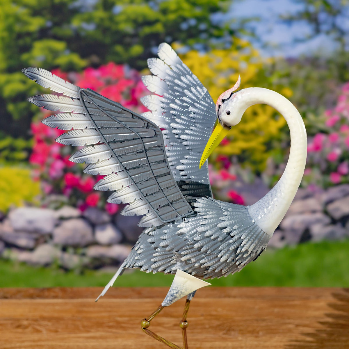 A metal heron bends its curved neck toward its chest, with one wing lifted above its back.