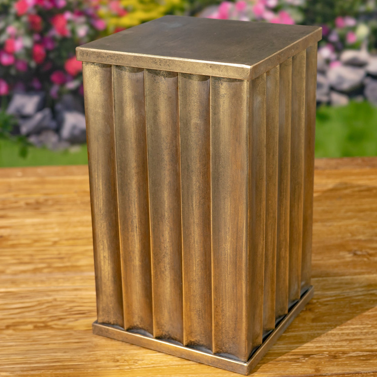 A bronze-toned fluted pedestal shown alone on a wooden surface.