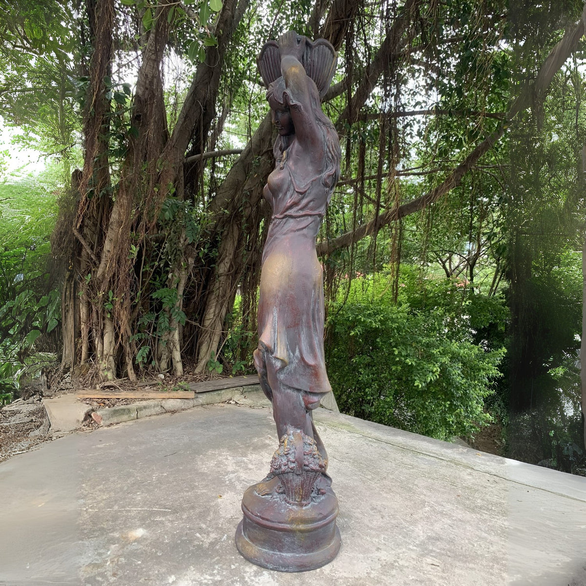 Side profile of the statue shows the woman's raised arms, flowing dress, and flower pot above her head.