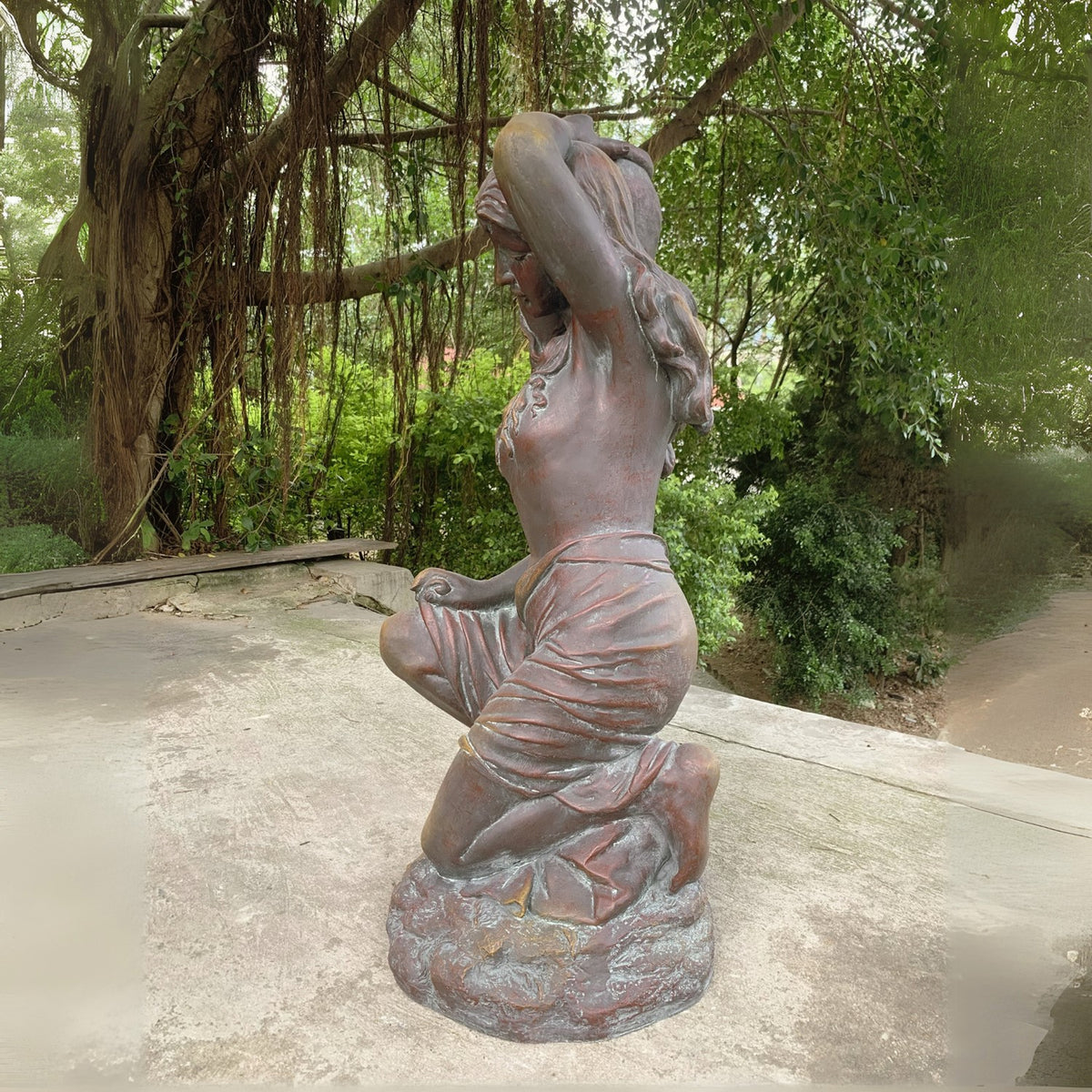 Kneeling woman statue in draped clothing, holding a large urn beside her shoulder beneath leafy trees.