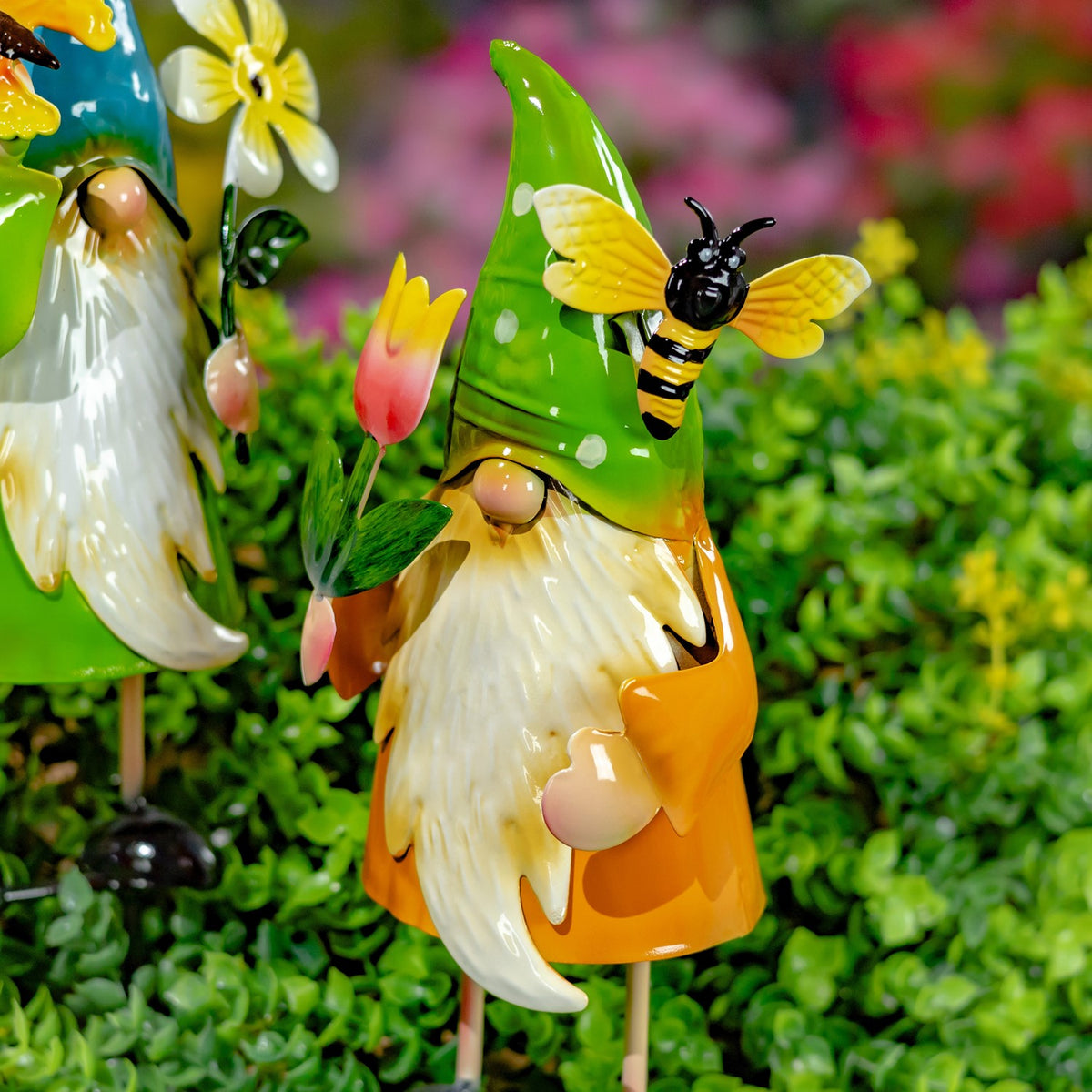 An orange-clad gnome in a green hat stands beside a bee and a pink tulip.