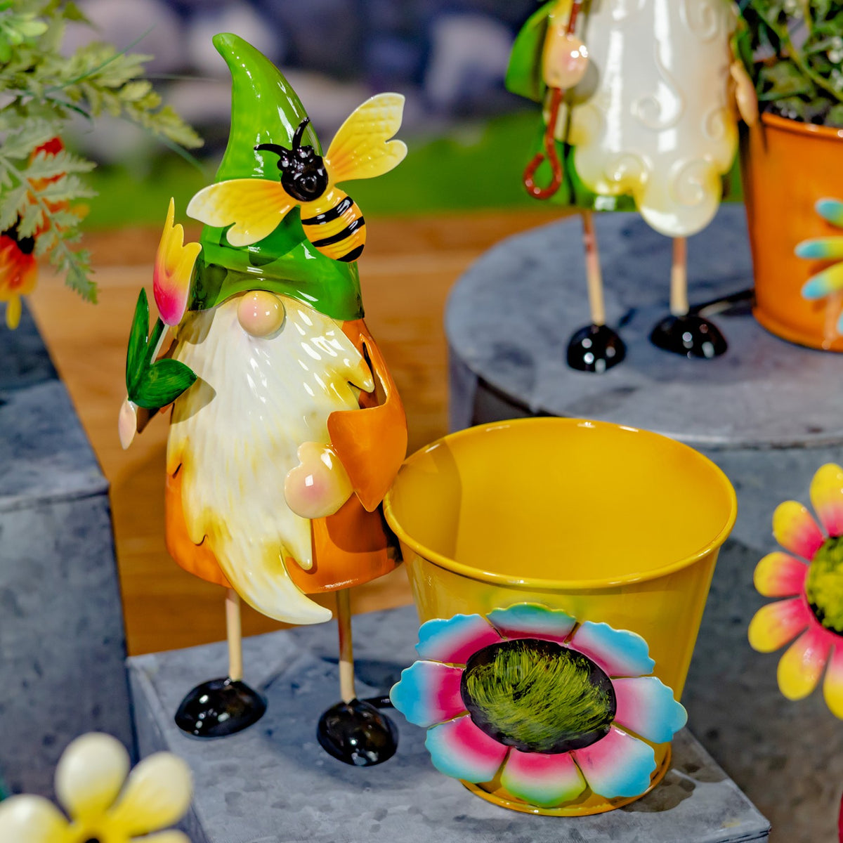 A yellow flower pot with a painted multicolored bloom beside a gnome with a bee on its green hat.