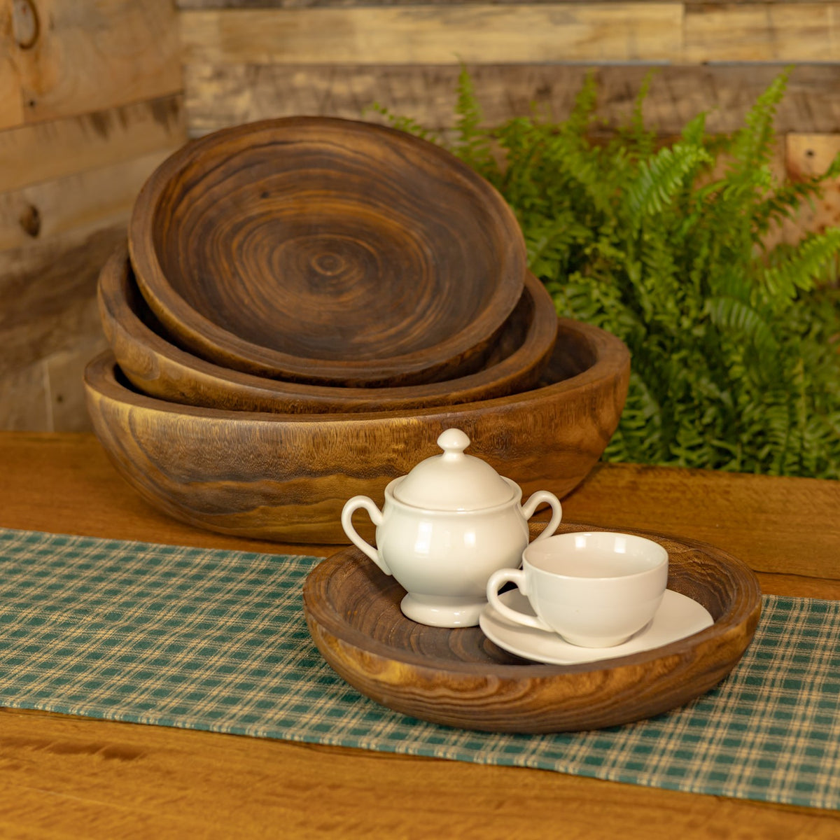 Nested wooden trays with a white teapot and cup arranged in the foreground tray.